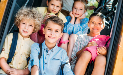 group of smiling schoolchildren sitting on stairs of school bus and looking at camera