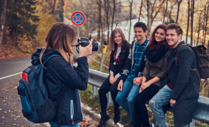Group of young friends with backpacks sitting next to a road in forest